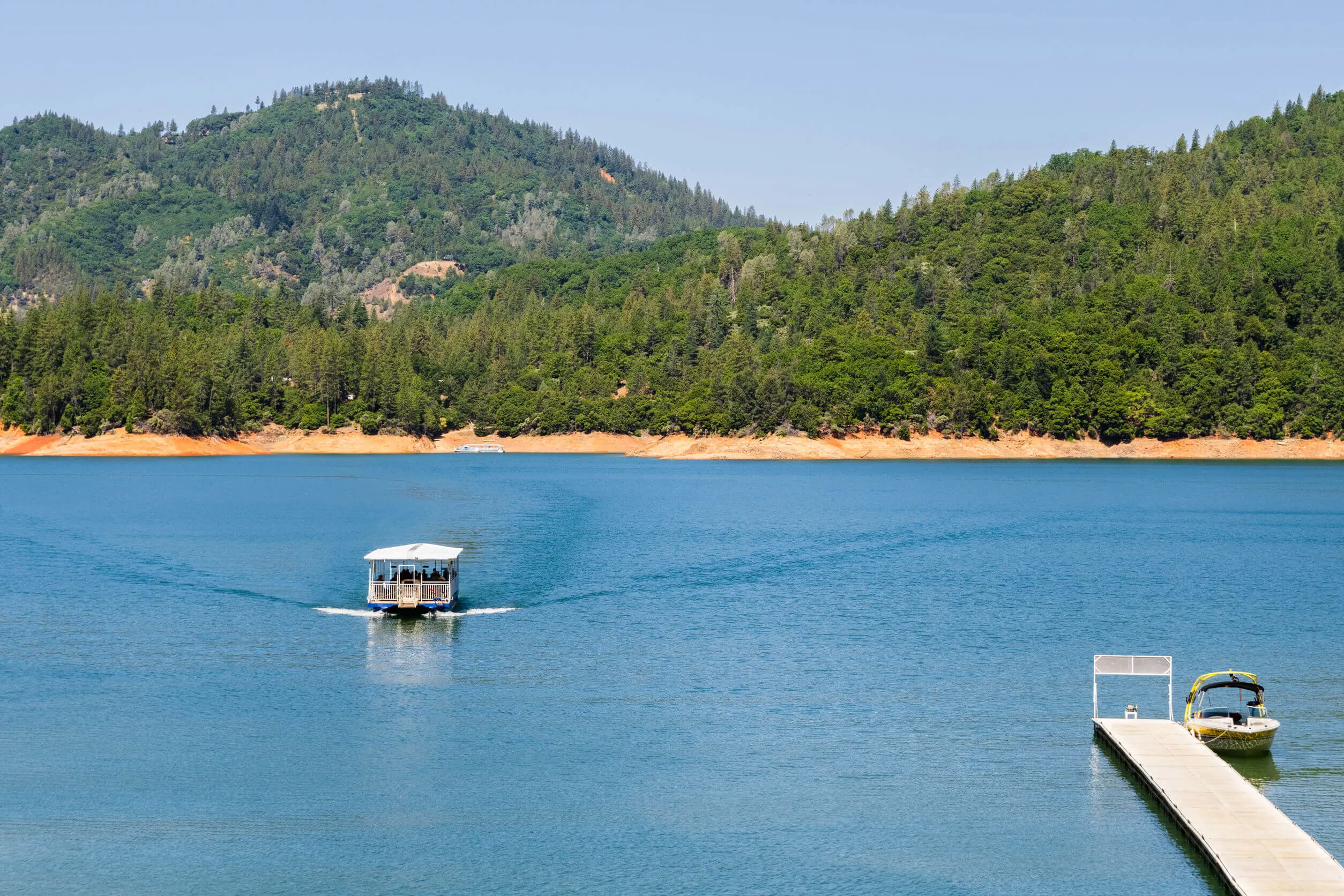 Shasta Lake, McCloud River Arm landscape on a sunny summer day with ship approaching the shoreline, Northern California